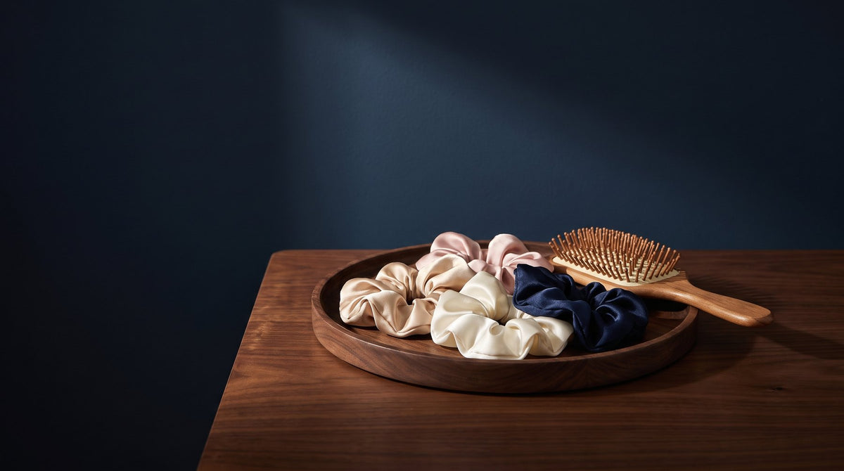 Silk scrunchies in soft neutral colors arranged on a linen cloth beside a hairbrush