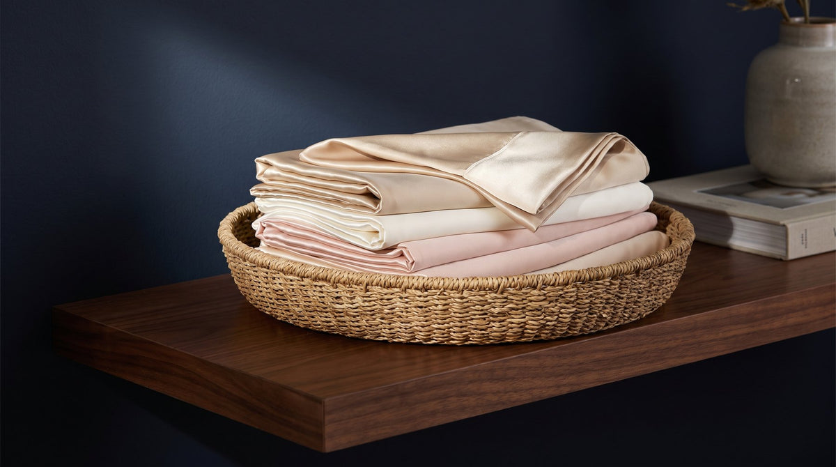 A folded mulberry silk pillowcase next to a mesh laundry bag and a bottle of gentle detergent