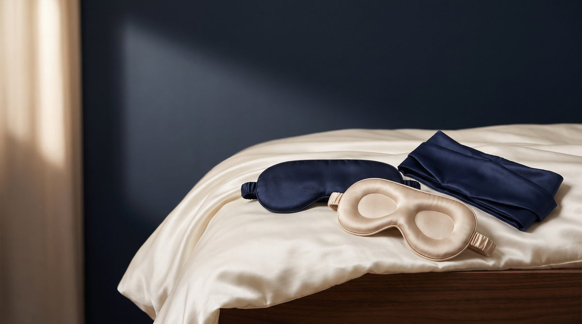 Three silk sleep masks, one contoured, one flat and one wide wrap style, laid side by side on a bed