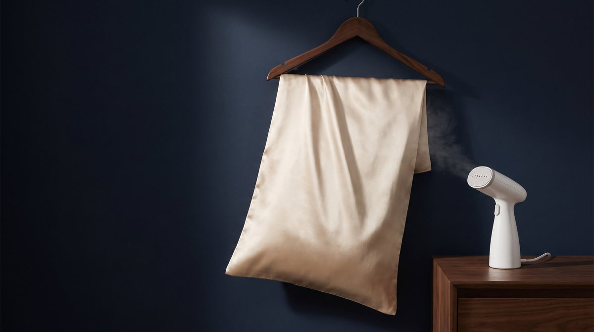 A lightly creased ivory silk pillowcase hanging on a wooden hanger beside a window in soft daylight