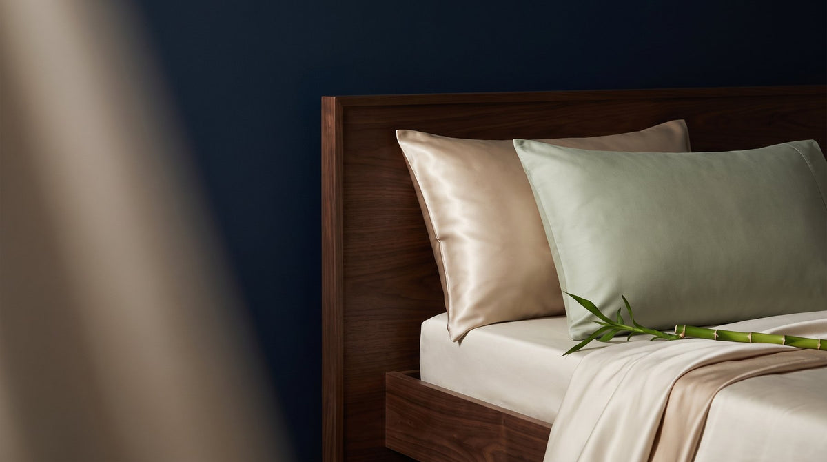 A champagne mulberry silk pillowcase and a matte white bamboo pillowcase laid side by side on a made bed