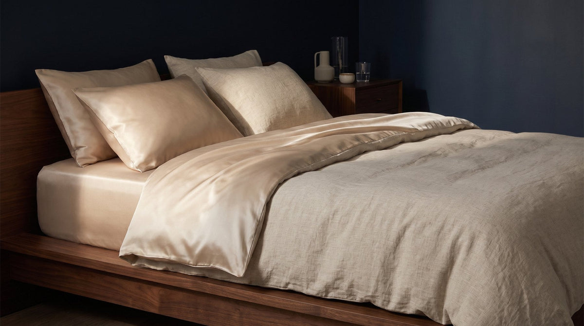 A bed made with a smooth ivory silk duvet cover folded back over rumpled natural linen sheets in soft morning light