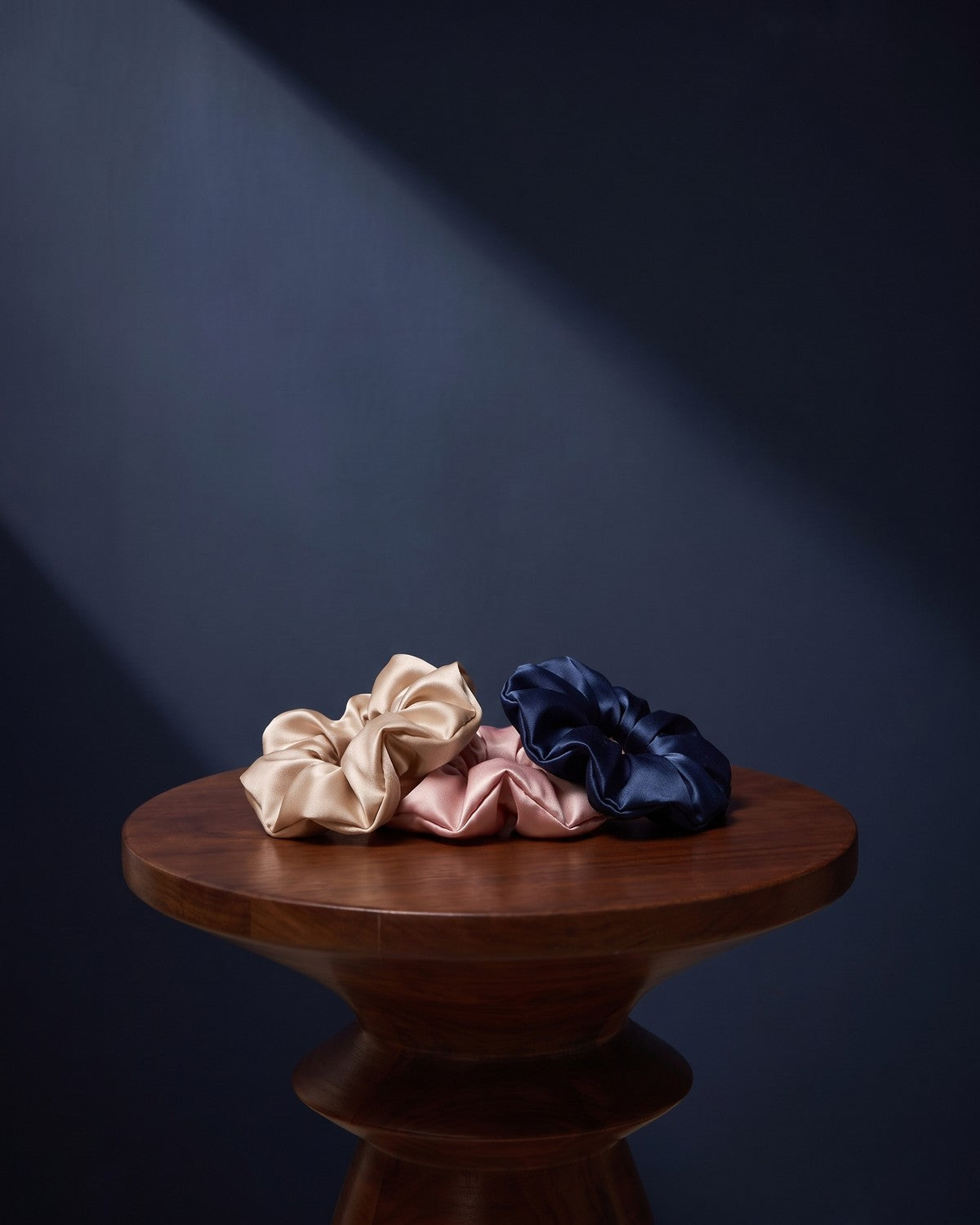 Three KINT silk scrunchies on a walnut side table