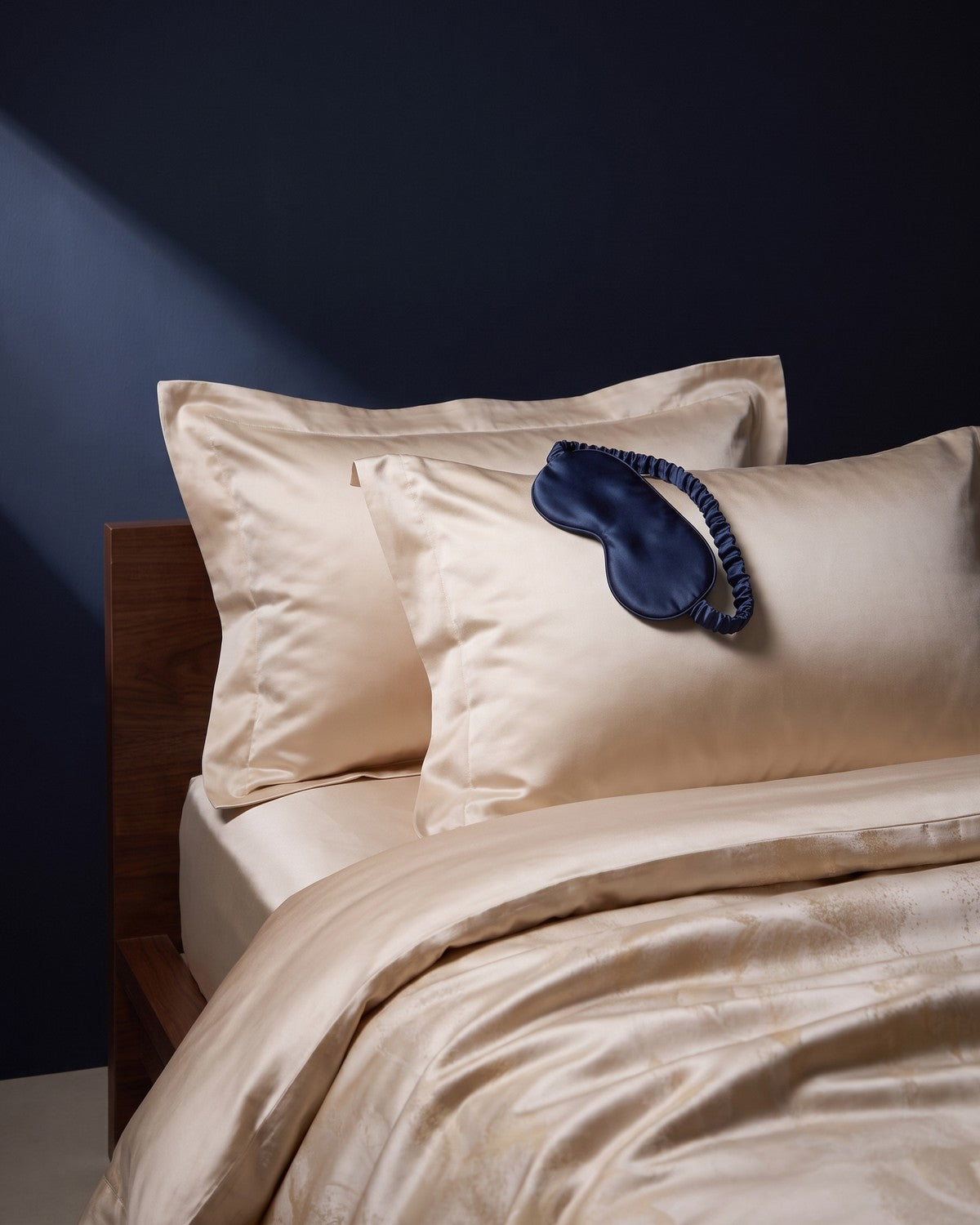 Woman in a slate blue silk pajama set sitting on a bed
