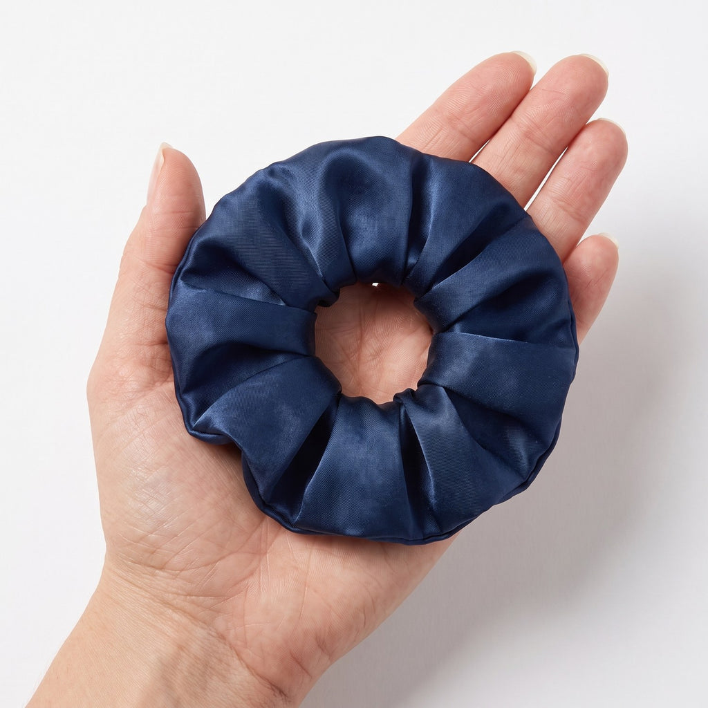 The large navy KINT silk scrunchie held in an open hand to show its size
