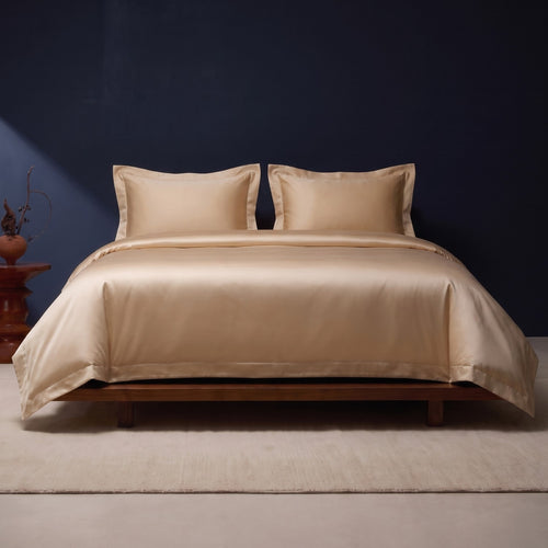 KINT silk and cotton satin bedding set in Light Gold on a low walnut bed against a navy wall