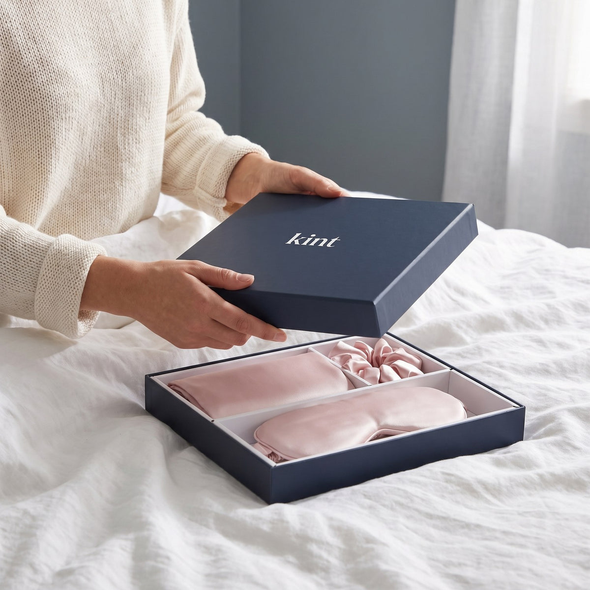 Hands lifting the lid of the navy KINT gift box with the silk set inside