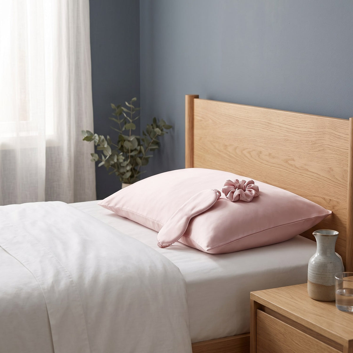 Blush pink silk pillowcase with the matching sleep mask and scrunchie on a bed