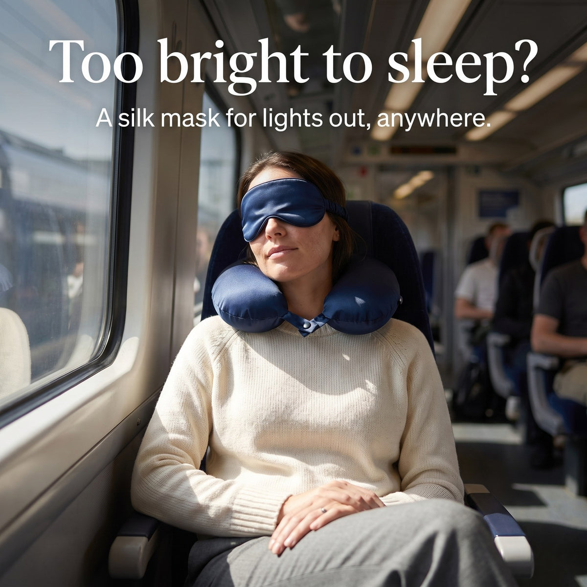 Woman resting on a bright train wearing the navy KINT silk sleep mask and neck pillow
