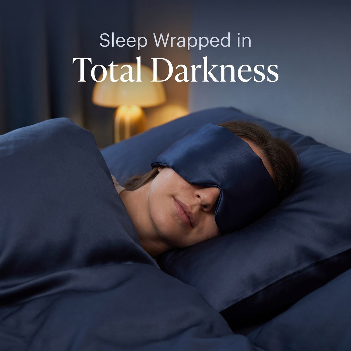 Woman asleep in navy silk bedding wearing the KINT silk wrap sleep mask