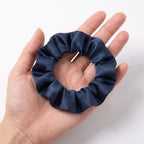The slim navy KINT silk scrunchie held in an open hand to show its size