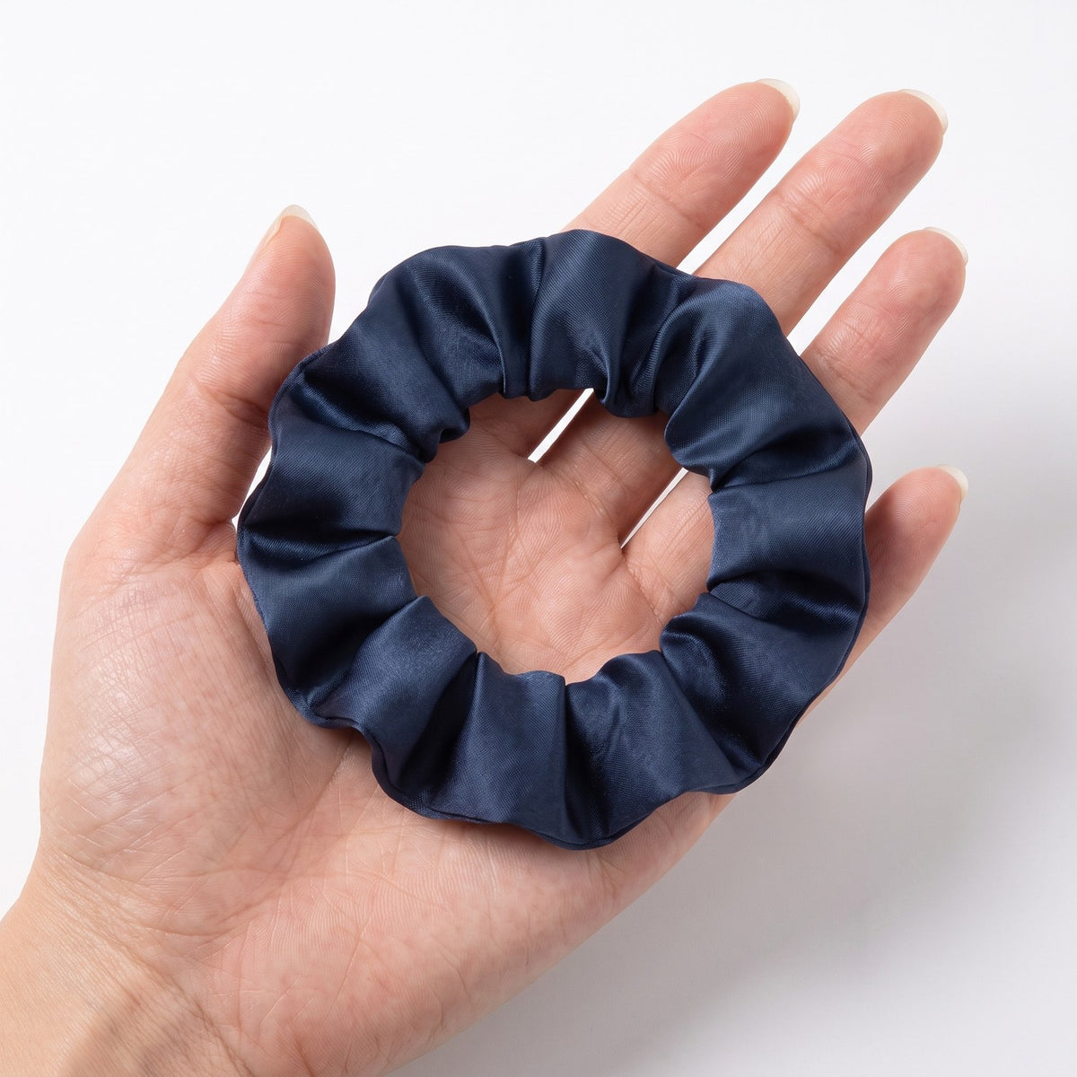 The slim navy KINT silk scrunchie held in an open hand to show its size