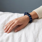 The slim navy KINT silk scrunchie worn on a wrist
