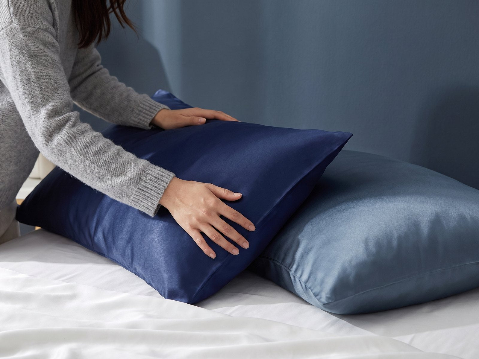 Hands smoothing a navy KINT silk pillowcase while making the bed