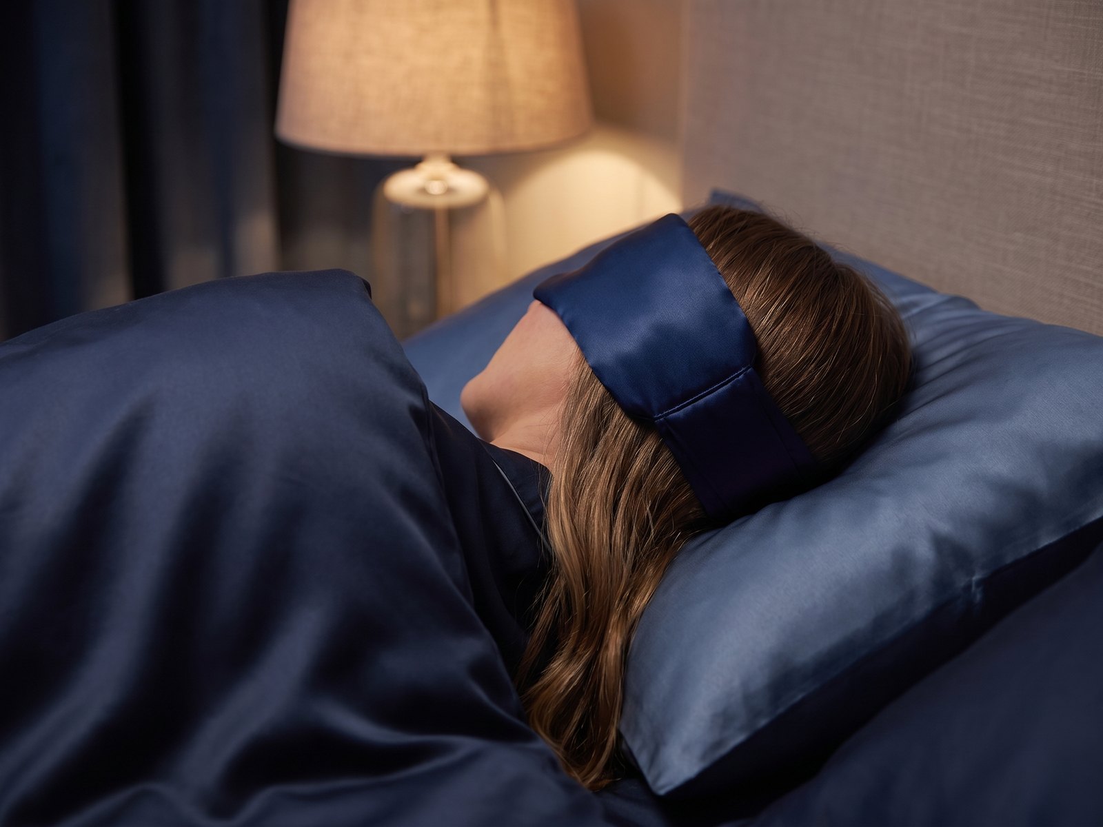 Woman asleep on her side wearing the KINT silk wrap sleep mask, fastened at the back